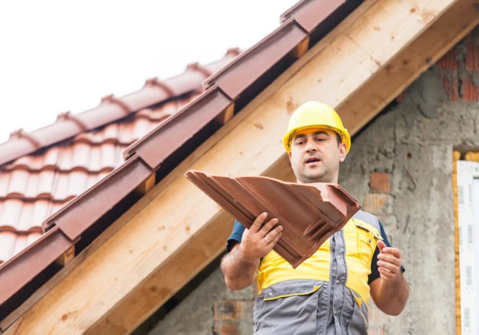 Building a roof on the house The builder stands on the background of a new building, holding a piece of tile in his hand